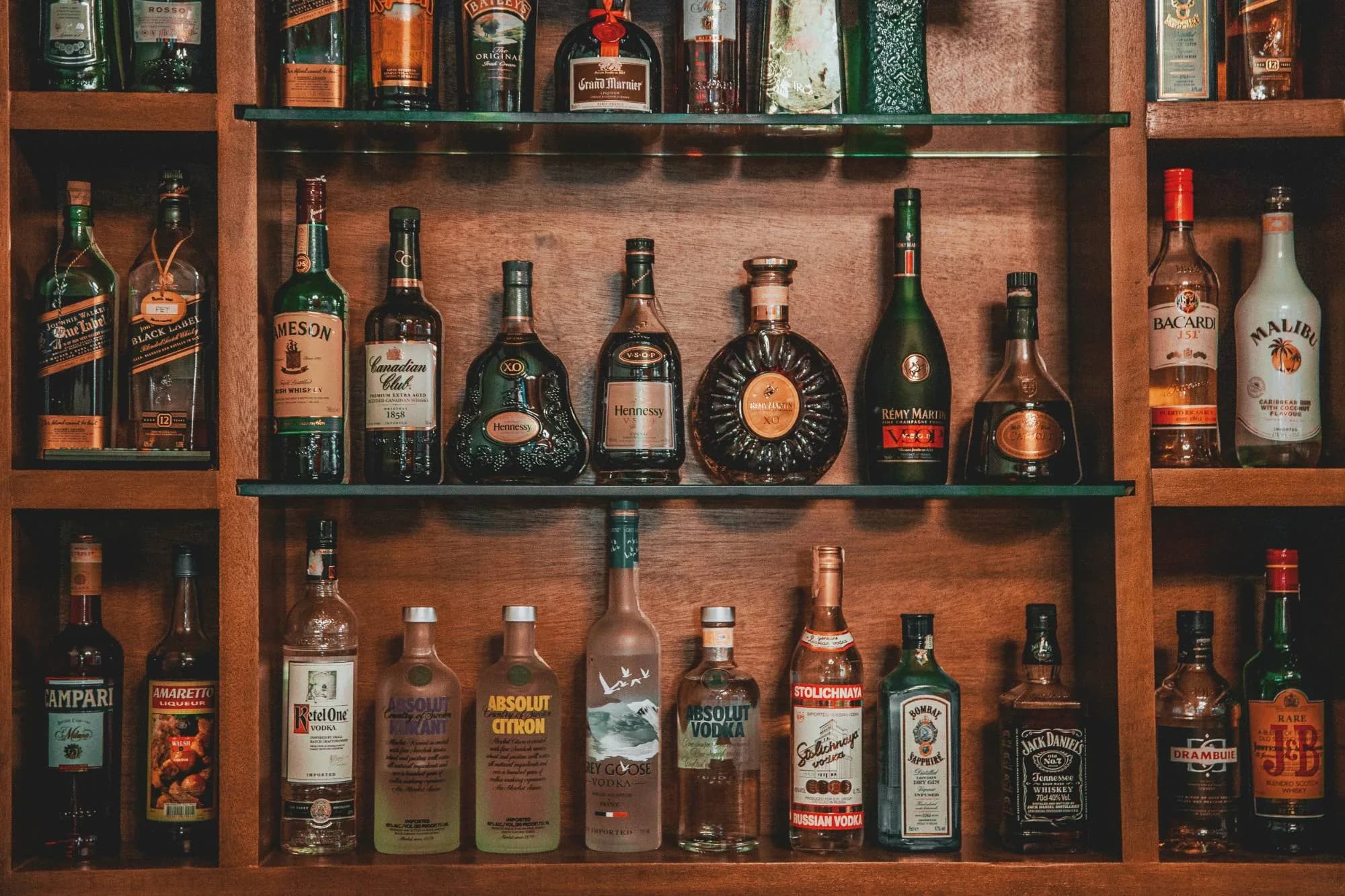 Wooden shelves of cognac, vodka, gin, and whiskey bottles